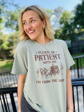 Load image into Gallery viewer, A woman wearing a green short-sleeved graphic tee with the text 'Please be patient with me I'm from the 1900's' printed on it, standing outdoors.
